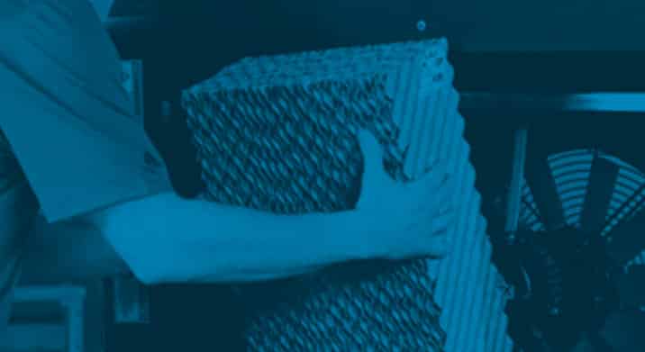 A person handles a large media pad for evap cooler, installing or extracting it from a machine, set against an industrial-themed blue monochrome background.