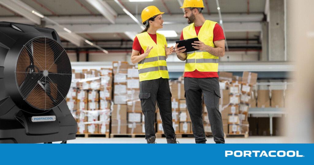 Two warehouse workers look at a tablet while being cooled by a Portacool evaporative cooler.