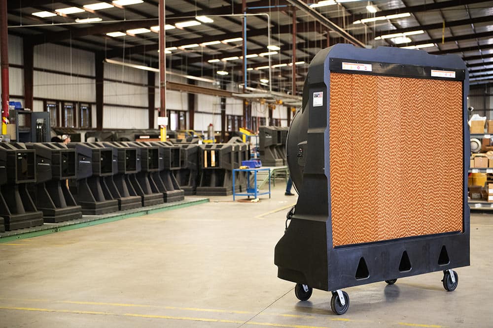 Industrial unit with honeycomb cooling pad on wheels in a spacious warehouse. Similar units line walls, creating efficient workspace with high ceilings.