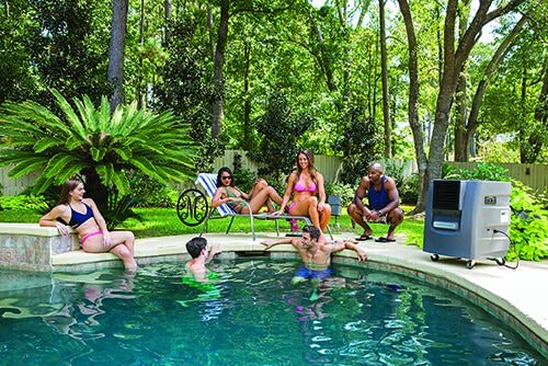 Six people relax by a pool amid trees, with some sitting on the edge and others in the water. Nearby, a pool heater enhances the casual summer vibe.