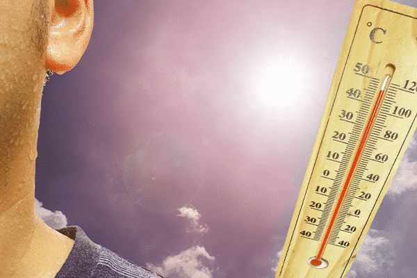 Close-up of a sweaty face next to a high-reading wooden thermometer, with the sun shining brightly in a partly cloudy sky.