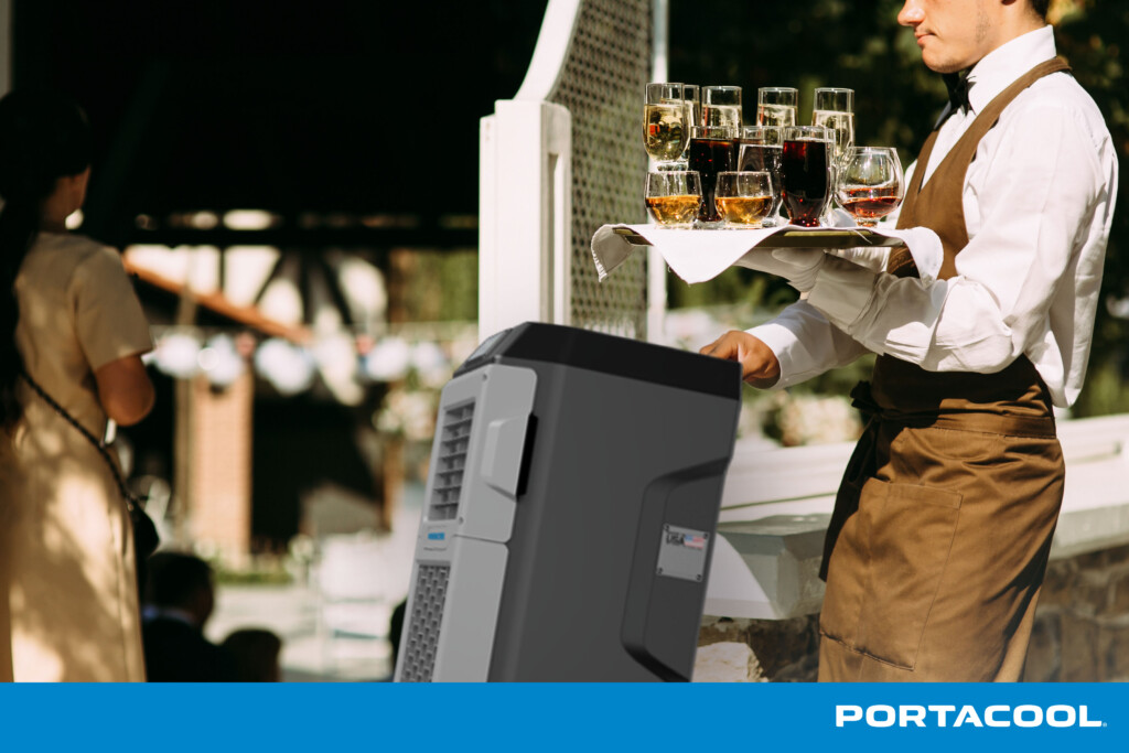 A waiter at a fine dining restaurant carrying a tray of drinks pushes a Portacool evaporative cooler ahead of him.