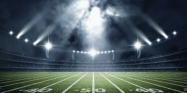 The football field is brightly lit under stadium lights, with distinct yard lines on turf. An empty stadium creates a focused, intense ambiance.