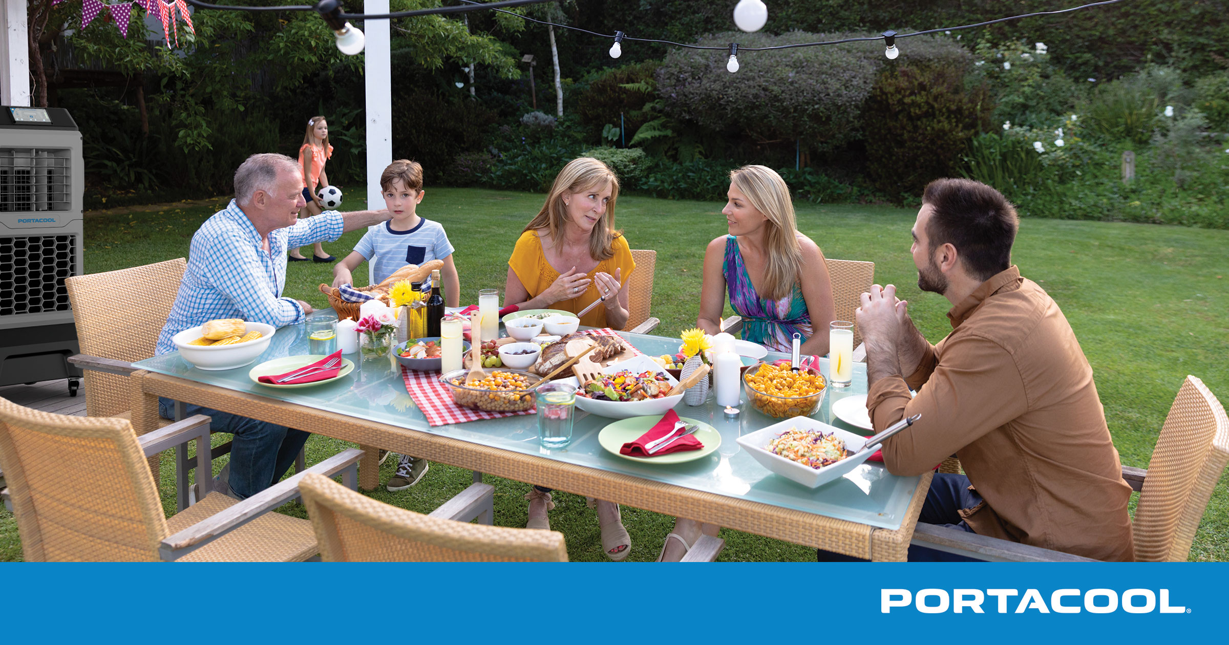 A family sitting around a table enjoying dinner on their patio, kept comfortable by their Portacool evaporative cooler.