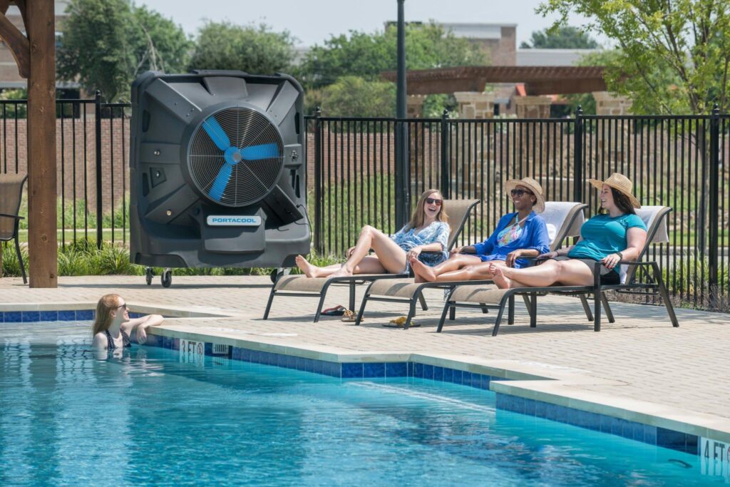 Four people lounge by the pool near a swamp cooler that is lowering the temperature.