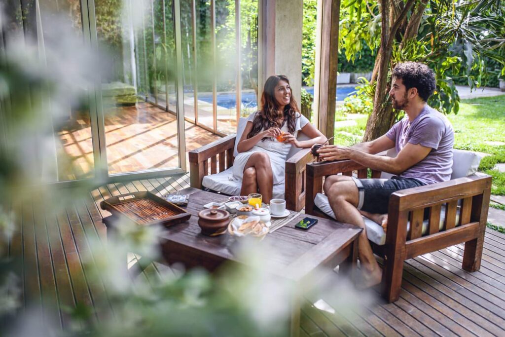 A man and woman sit on the porch talking about How do I keep my patio cool in the summer.