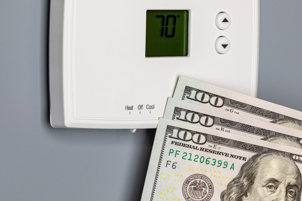 Thermostat with cash in front while answering how much does air conditioning cost to run.