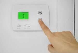 Person adjusting thermostat with a dollar sign, because they learned how much does air conditioning cost to run.