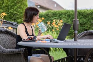 Woman searching on a laptop do swamp coolers work on a patio, sipping a drink and sitting outside.