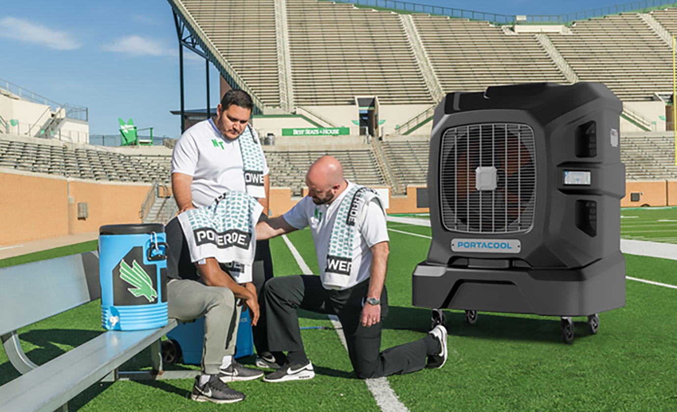 Two men, in white shirts and black trousers, assist a seated person on a football field. A Portacool and cooler are on the bench. Stadium seating in back.