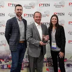 Three people in business attire stand smiling with a glass PTEN Innovation Award, in front of a PTEN logo backdrop.