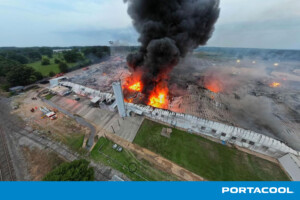 Portacool facility in Center, Texas, engulfed in flame. A huge plume of black smoke escapes the roof while visible flames consume the building.