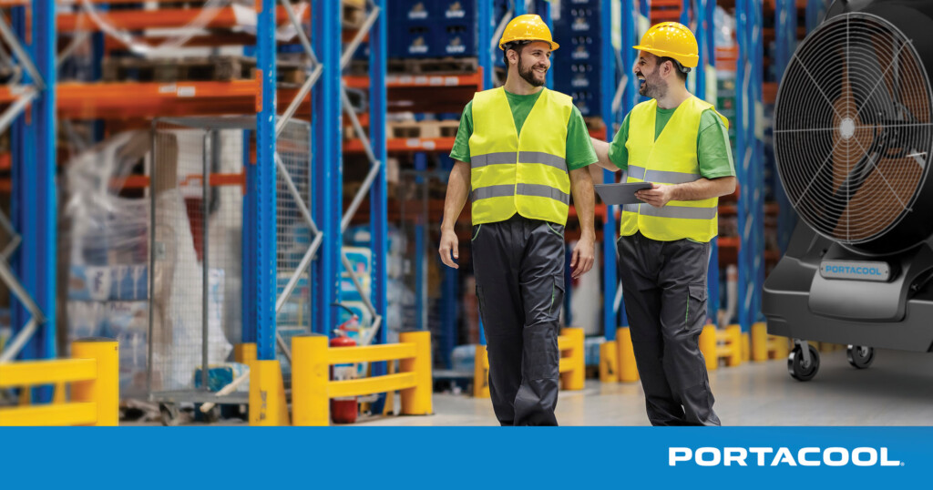 Two workers in PPE walk through a warehouse, kept comfortable by Portacool evaporative cooler in the background.