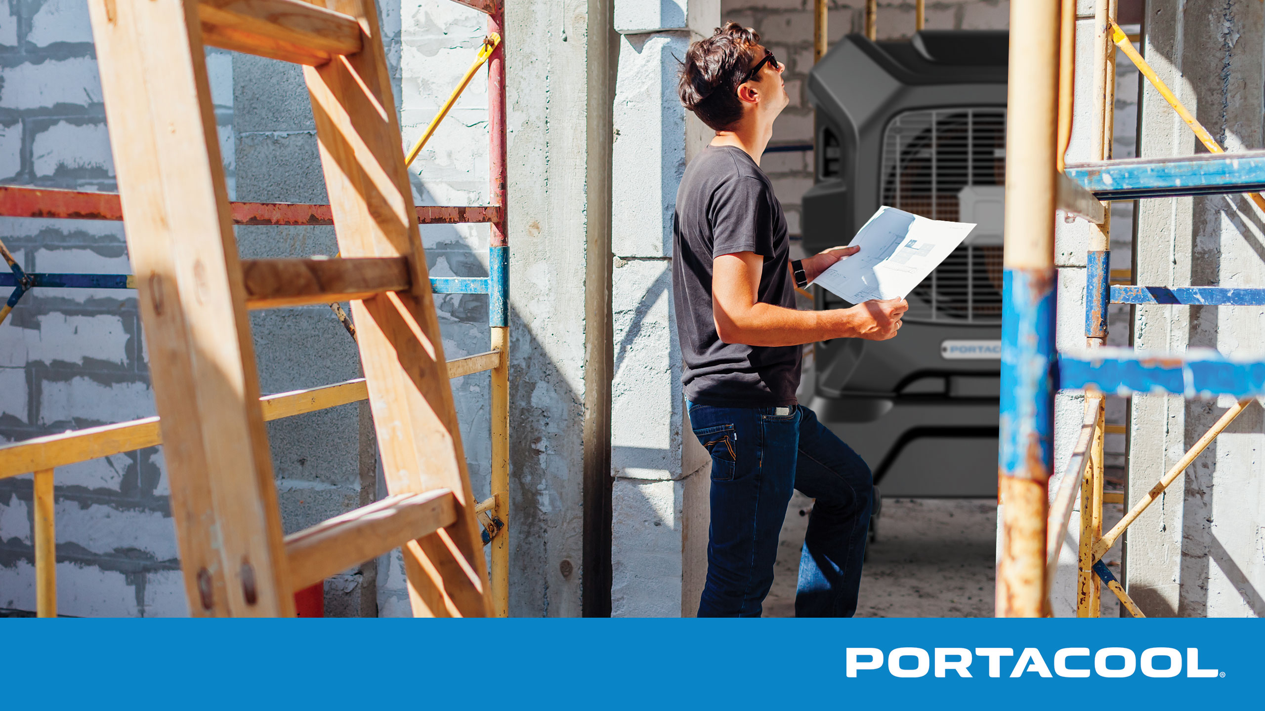 a man standing and holding blueprints in a construction site with a Portacool APEX evaporative cooler in the background.