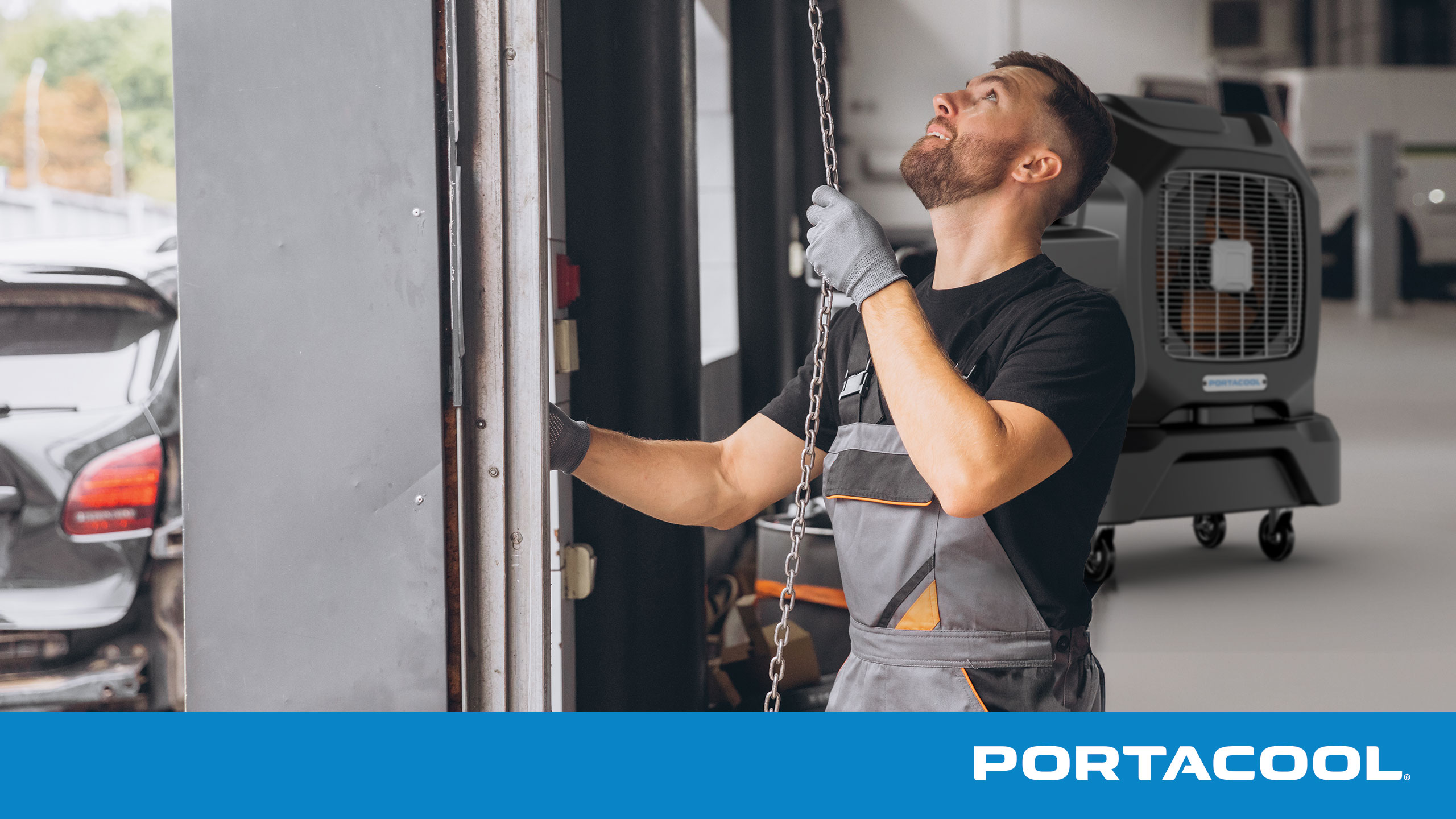 An auto technician opens a bay door to the auto shop with a Portacool evaporative cooler in the bakground.