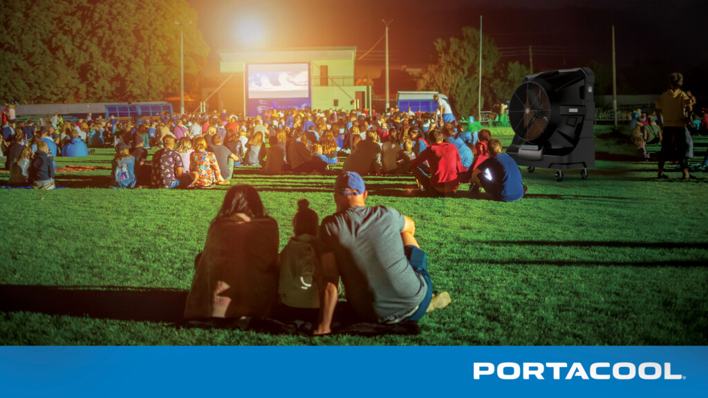 A family gathers to watch a movie outdoors on a hot summer evening during a community event, kept cool by a Portacool portable evaporative cooler.