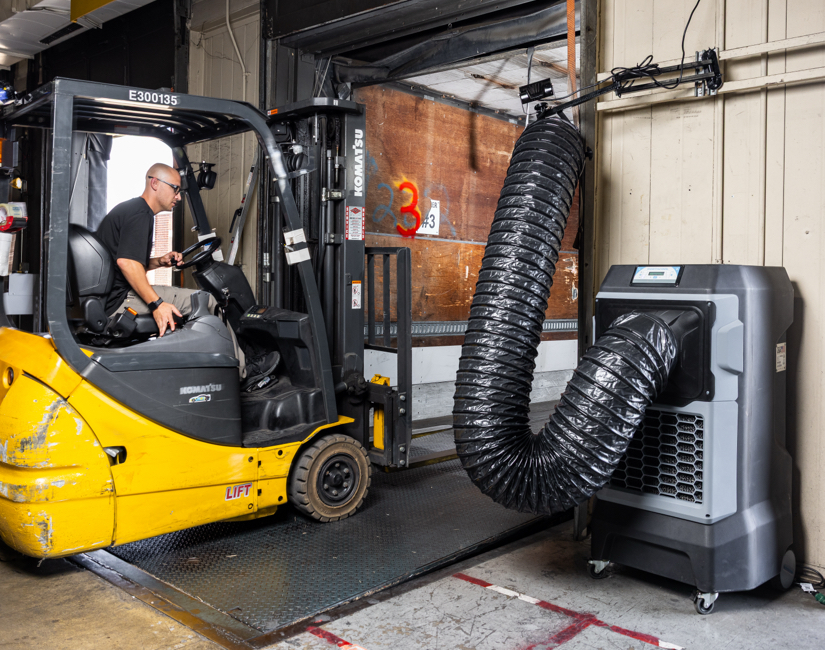 A Portacool APEX 700 with a VORTEX precision cooling kit at a loading dock lowers the temperature inside a trailer while a warehouse worker operating a forklift enters.